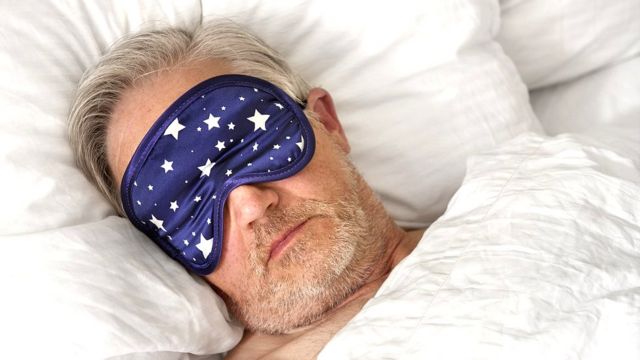 Man in bed wearing sleeping mask.