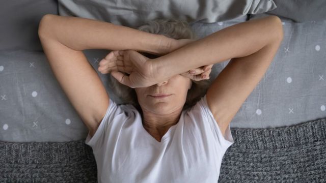 Woman in bed having trouble sleeping, covering her eyes with her arms