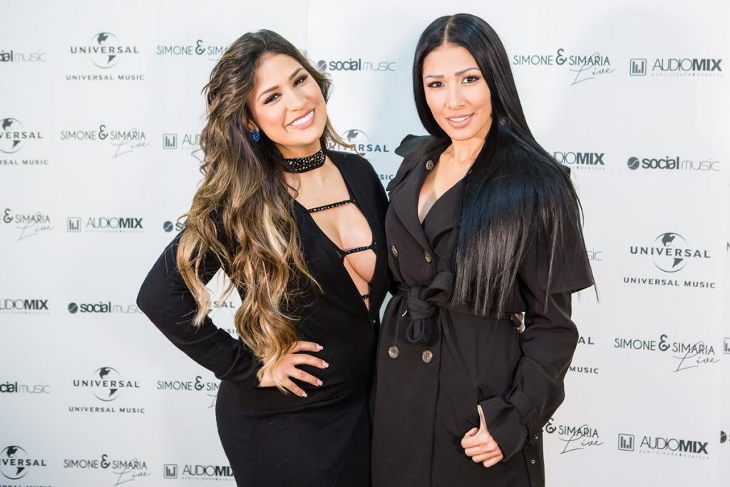 Country singers Sisters Simon and Simaria pose for a photo in a box for the duo's tour.  They wear tight black dresses, have olive skin and long dark hair.