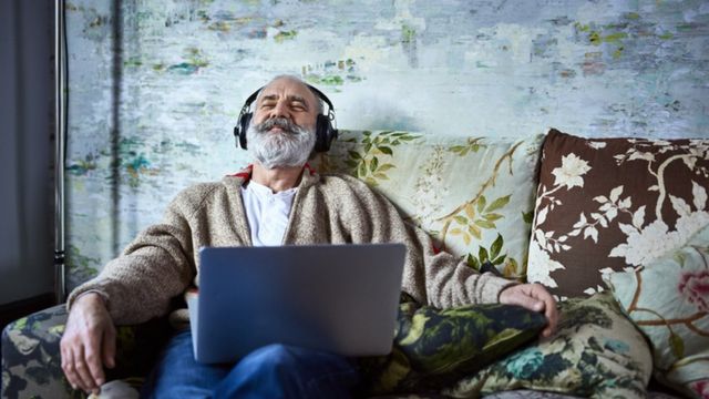 Man sitting on sofa with laptop on lap listening to music