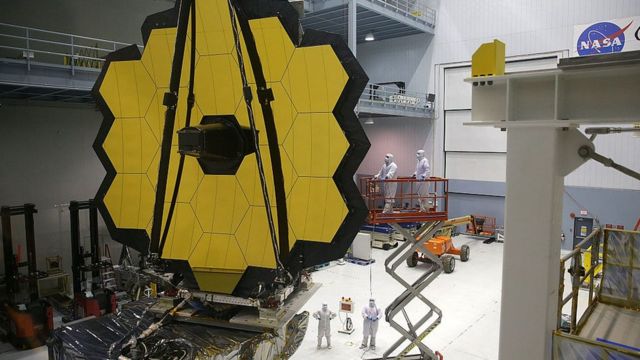The James Webb Telescope in a large room, with people in lab coats working around it